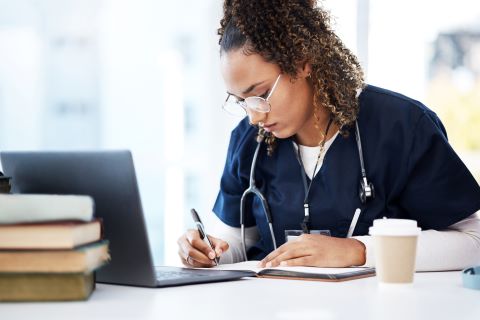 A nurse in front of a computer, writing in a notebook.