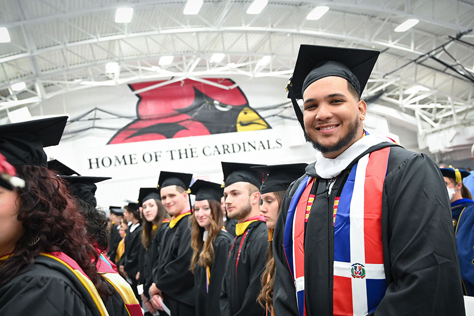 A Fisher graduate smiles in his cap and gown during Commencement..