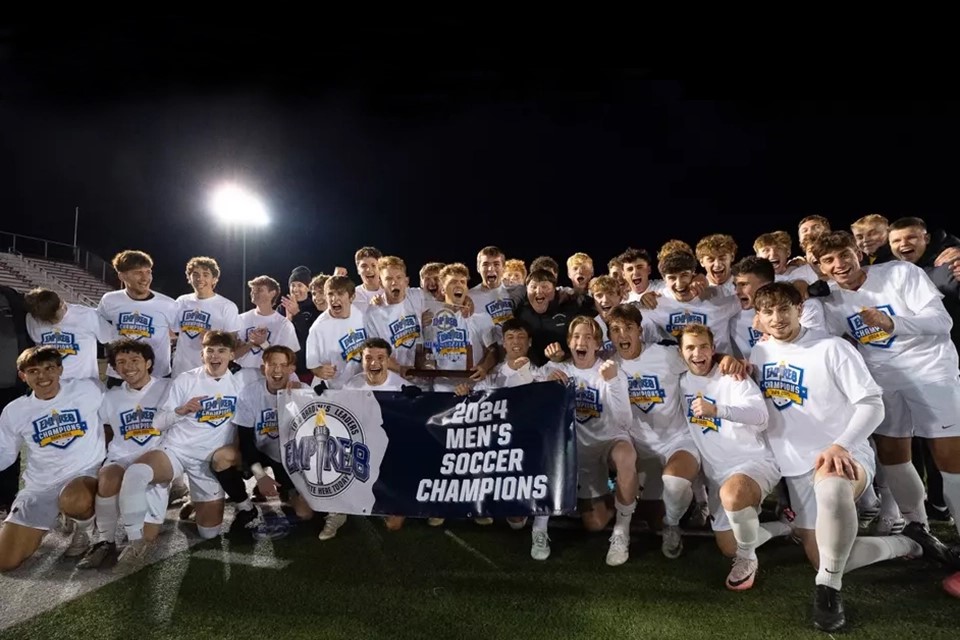 The men's soccer team holds up the Empire 8 Championship banner.