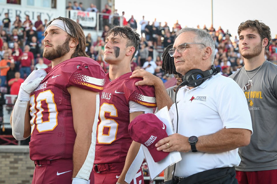 Coach Paul Vosburg stands on the sidelines with two Cardinal football players.