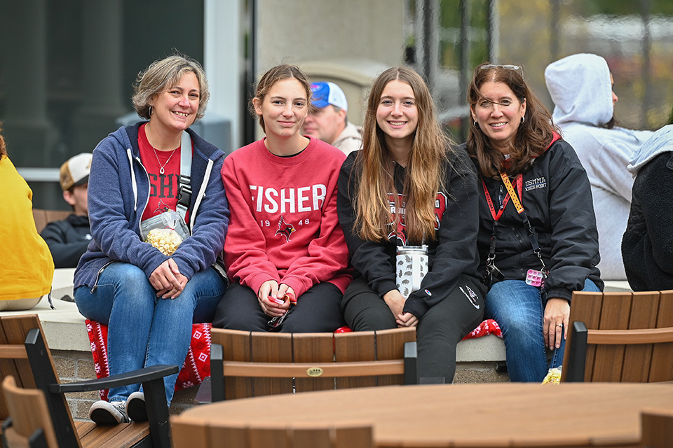 A family of four in Fisher gear sits along the firepit at the Terrace at Tepas Commons during Family Weekend 2023