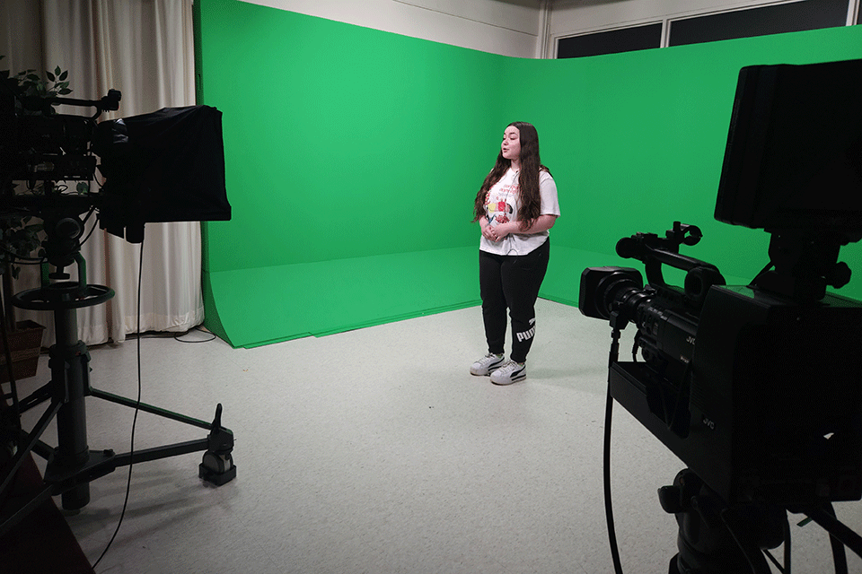 A student practices speaking in front of a camera in the Cardinal Television studio.
