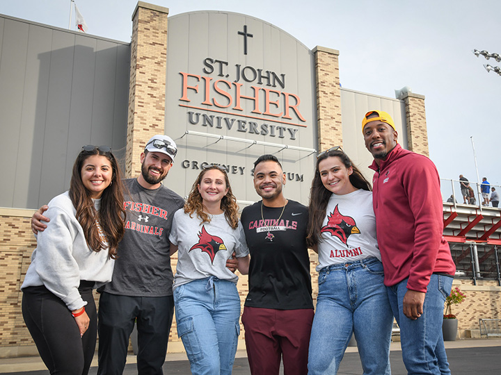 A group of Fisher graduates stand together outside of the St. John Fisher University Growney Stadium