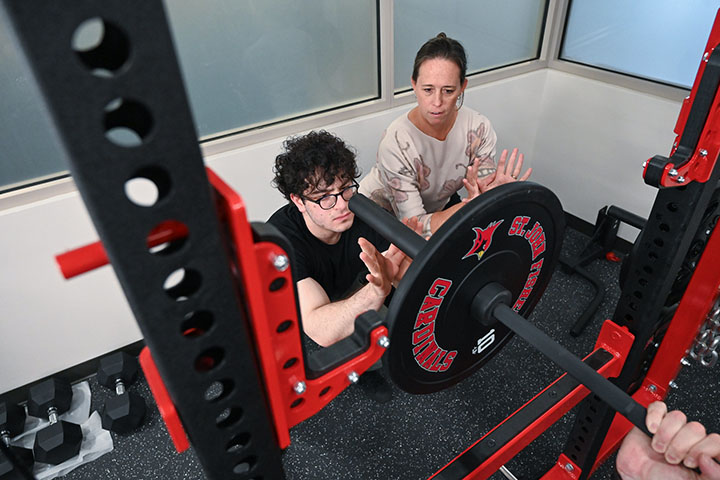 A professor models how to spot for a weightlifter in the athletic performance lab.