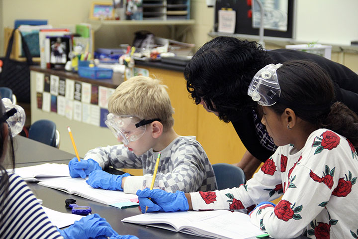 Teacher bending over to speak with two students working on a science project.