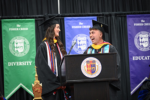 Two graduating students laugh together at the podium while giving a Commencement speech.