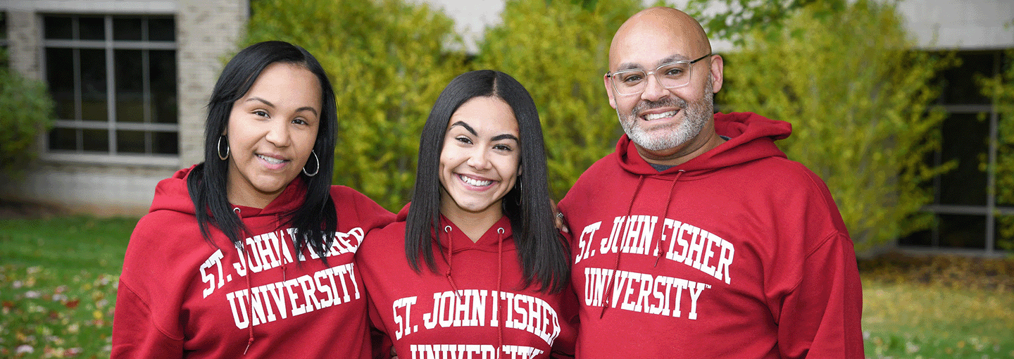 A family of three wearing matching St. John Fisher University sweatshirts.