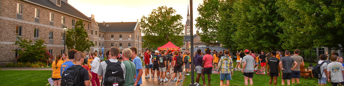 Students mingle on campus with the sun setting in the background.