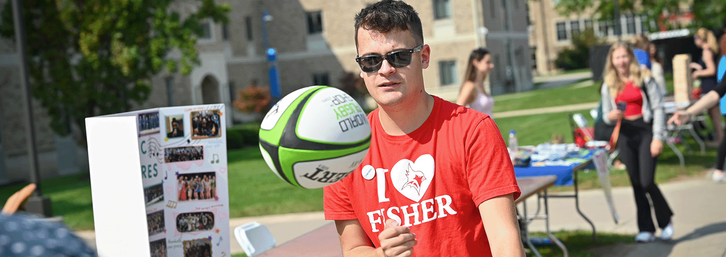 A student catches a rugby ball while wearing an I Heart Fisher shirt.