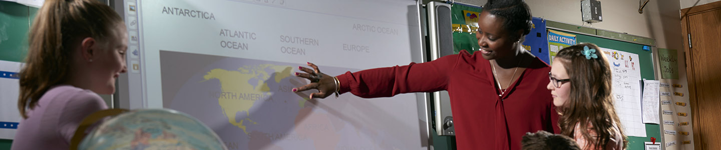 A teacher shows to a world map to three young students.