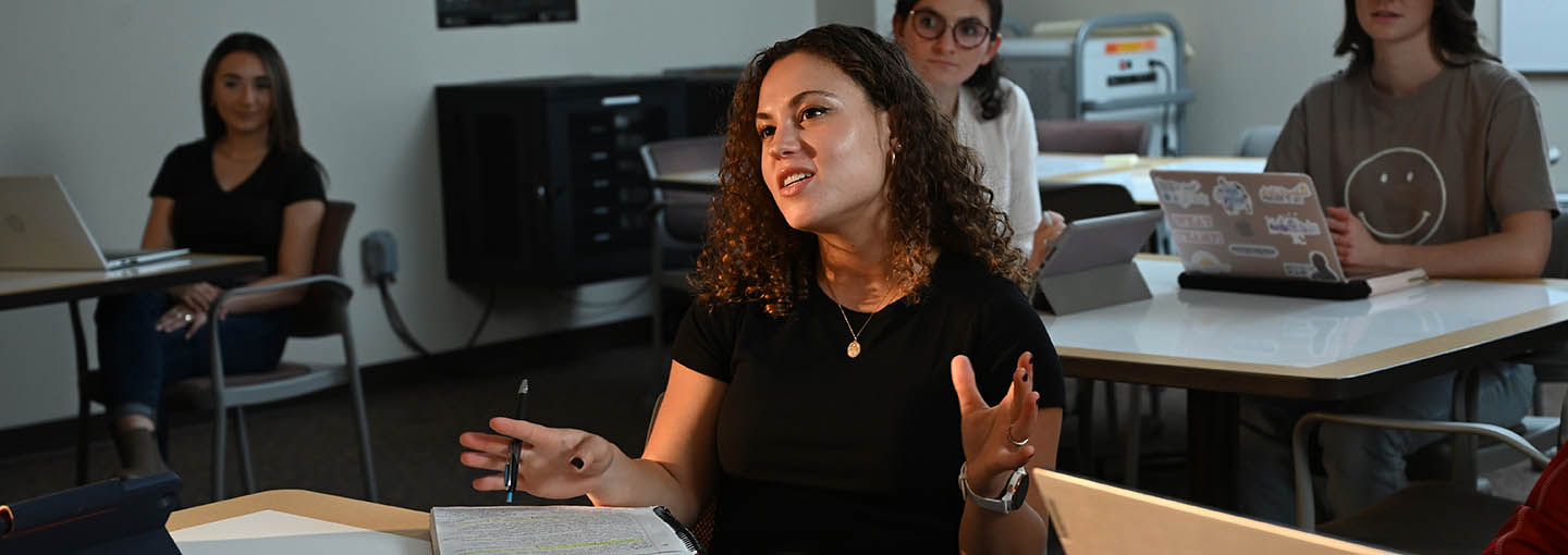 A female graduate student sitting in a classroom talking.