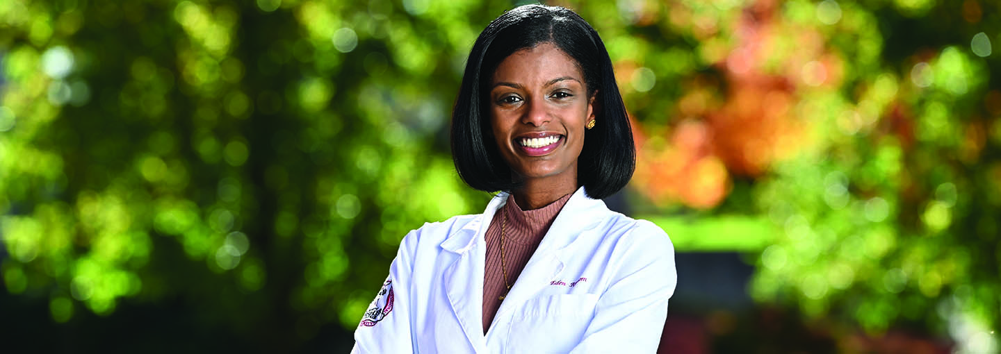 A smiling pharmacy student in her white coat standing outside.