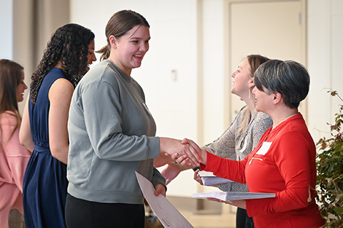 A student receiving a scholarship shakes a University leader's hand.