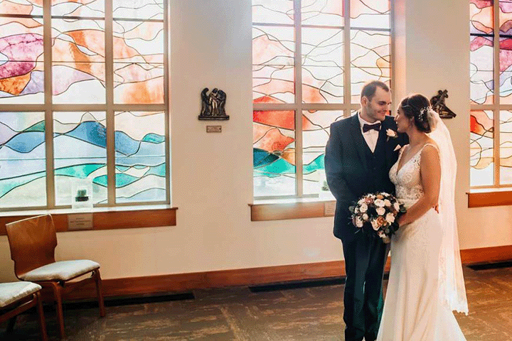 A couple with stained glass windows of the chapel as the backdrop on their wedding day.